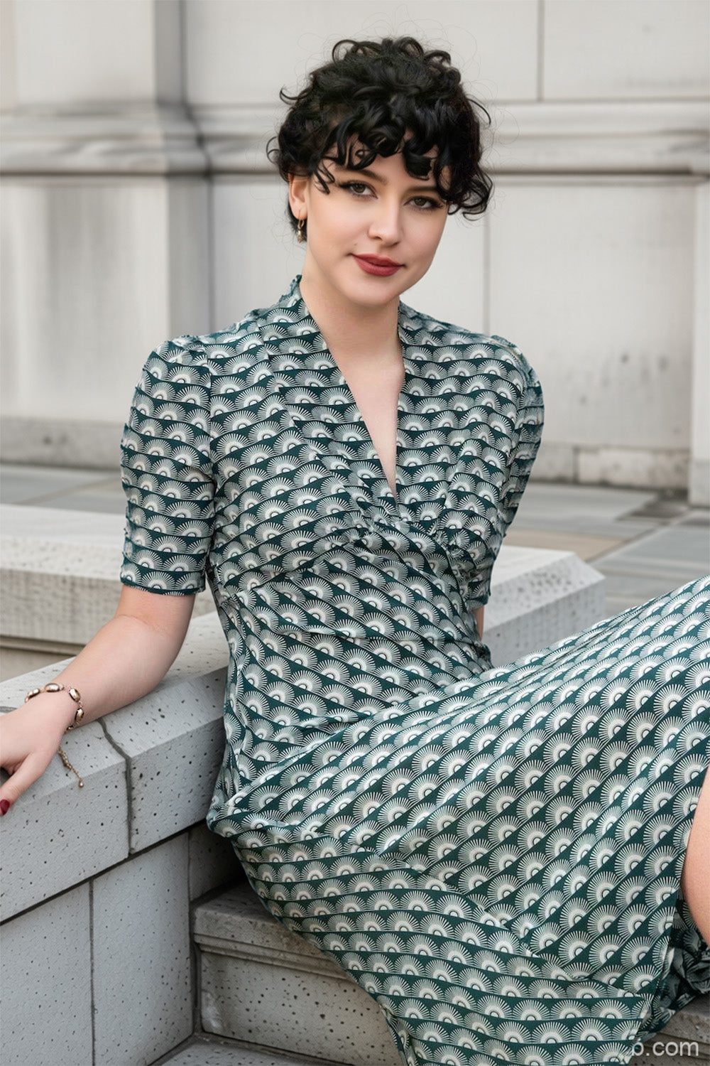 1940s green print dress worn by model sitting on a stone step